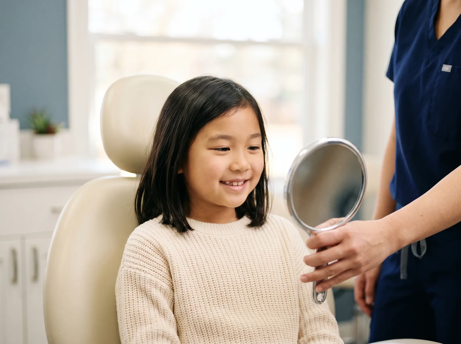 A child in the dental chair looking into a hand mirror